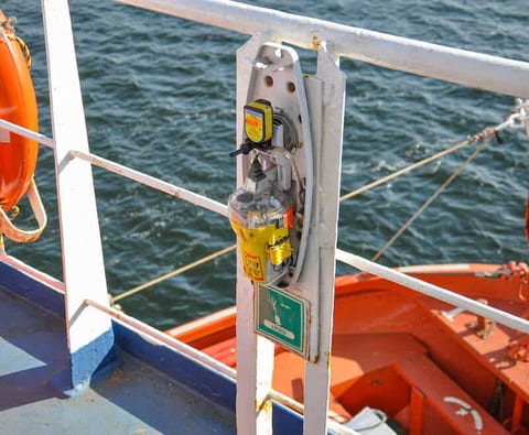 Float free EPIRB stowed in its hydrostatic release bracket on a ship railing beside the EPIRB station sign