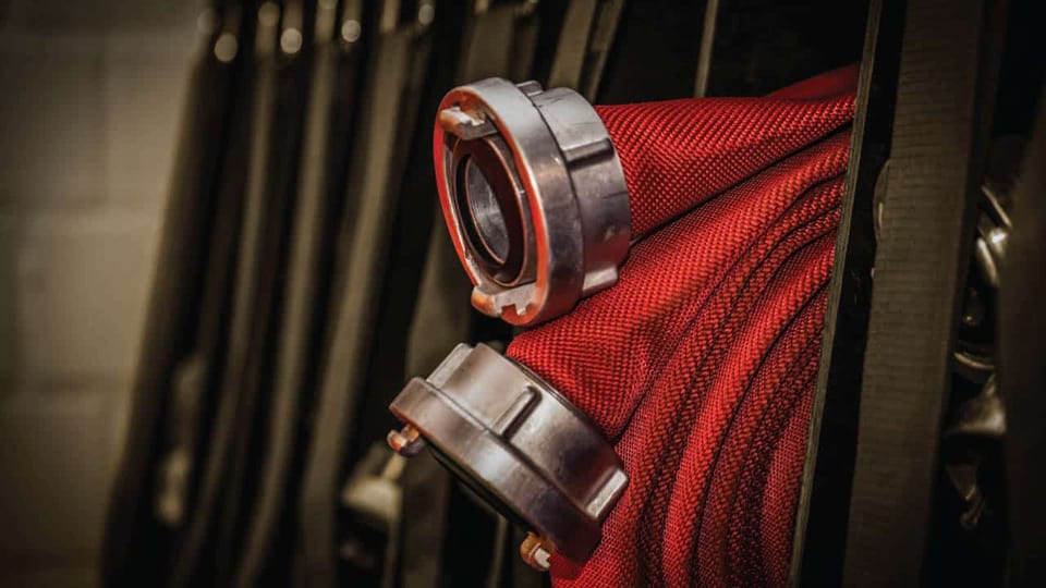 Folded red fire hoses with chrome couplings hanging in a shipboard rack