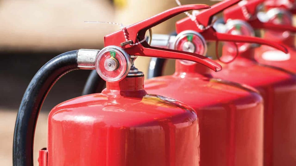 Row of red portable fire extinguishers with pressure gauges and discharge hoses