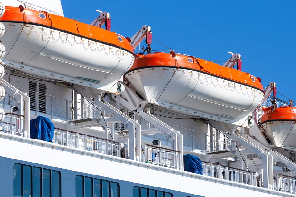 White partially enclosed lifeboats with orange covers hanging from davits on a passenger ship's boat deck