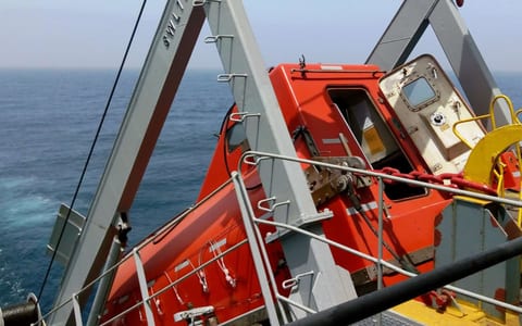 Davit launched totally enclosed lifeboat stowed at a ship's side with its hatch open