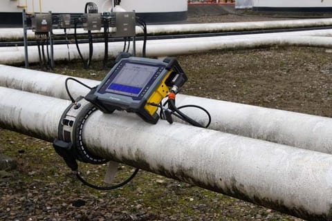 Guided wave testing collar clamped around a pipeline with a portable instrument displaying signal data