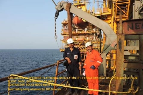 Two offshore technicians on a platform deck beside a lifeboat davit during witnessed load testing