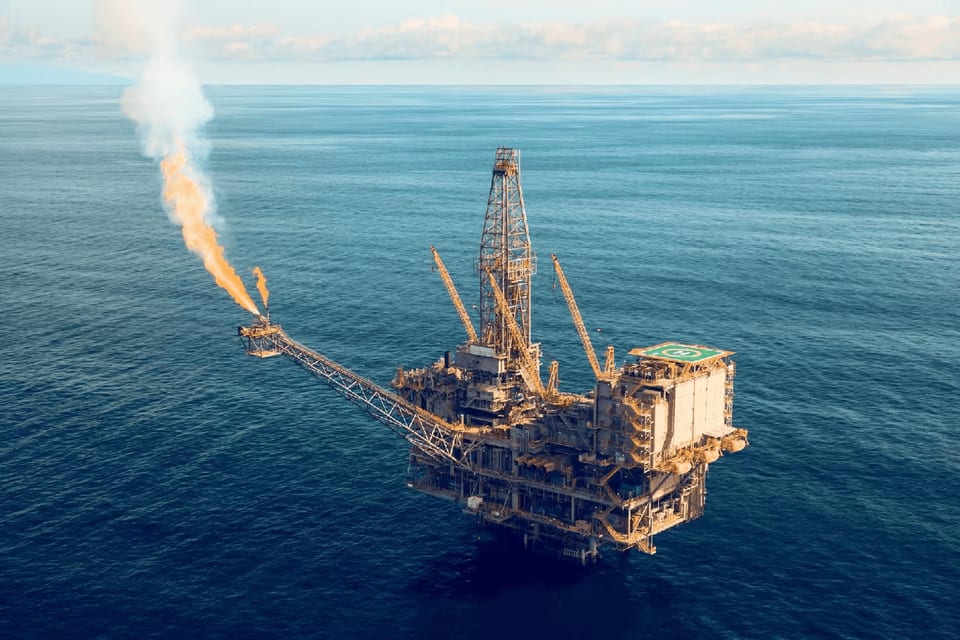 Aerial view of an offshore production platform flaring gas from its flare boom at sea