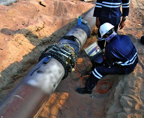 Technicians screening an excavated pipeline with a segmented ultrasonic transducer ring and a field laptop