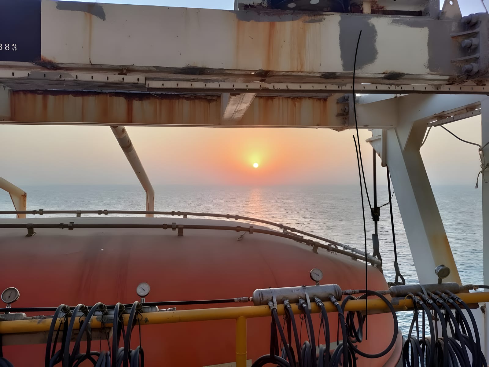 Sunset over the sea from an offshore platform deck, a lifeboat stowed in its davit below